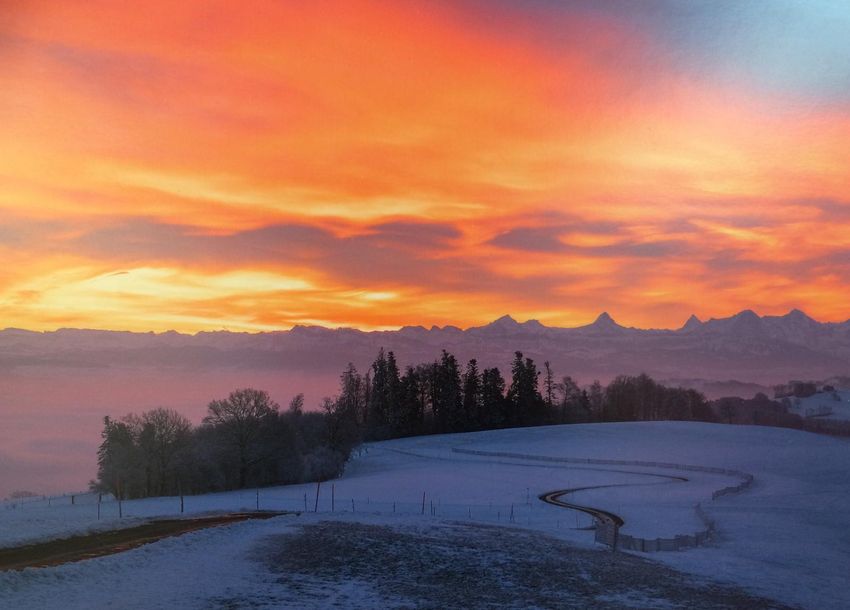 Sonnenuntergang mit Abendrot über einer verschneiten Bergkuppe mit Nebelmeer.